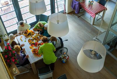 Gemeinschaftsraum in Seniorenbegegnungsstätte mit 6 gemeinsam am Tisch sitzenden bastelnden Senioren