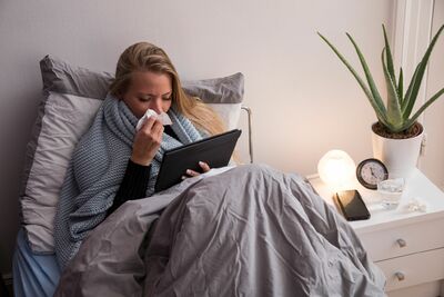 Erkältungskranke Frau insormiert sich online im Bett sitzend