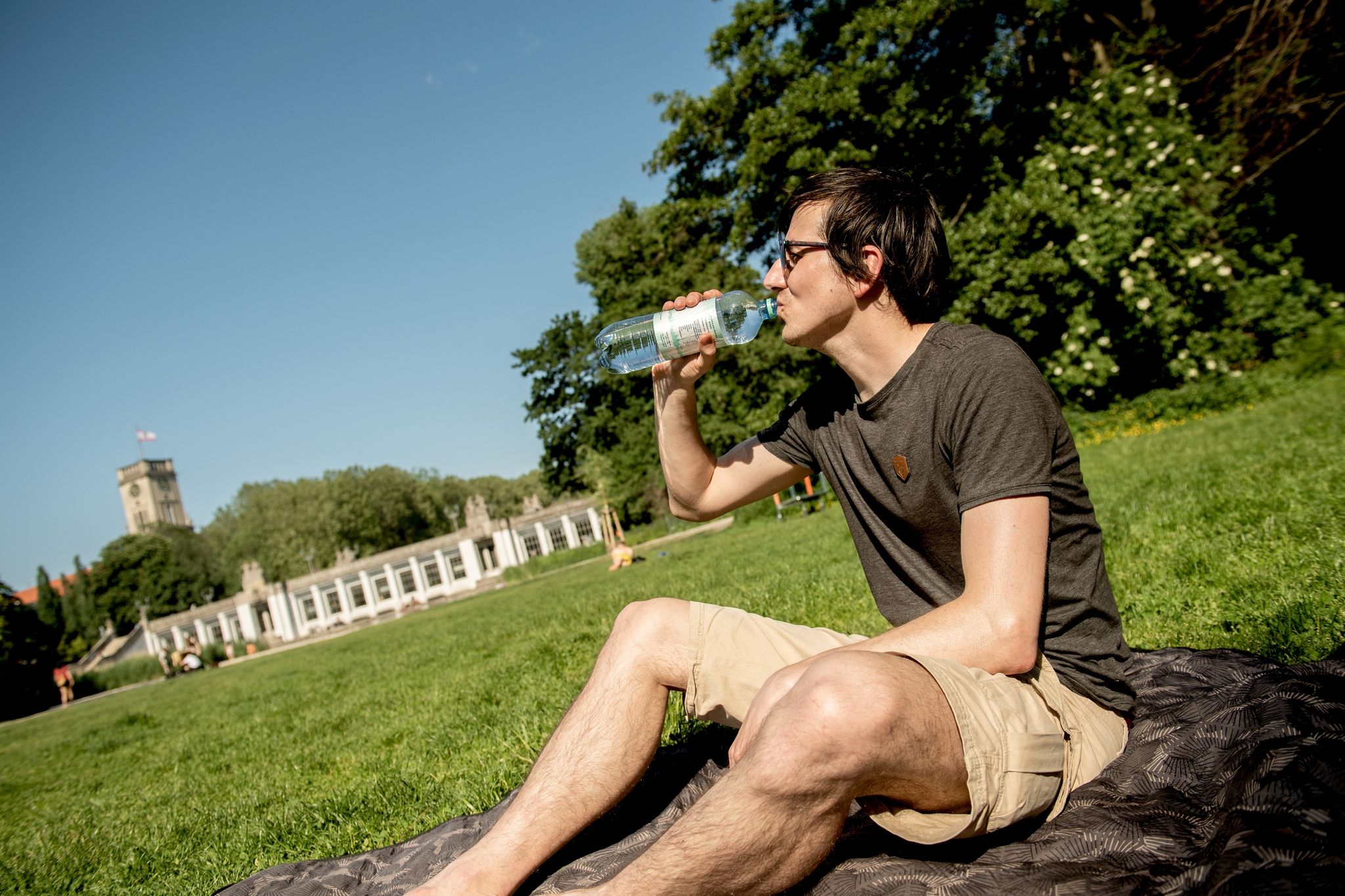 Mensch trinkt auf sommerlicher Grasfläche Wasser