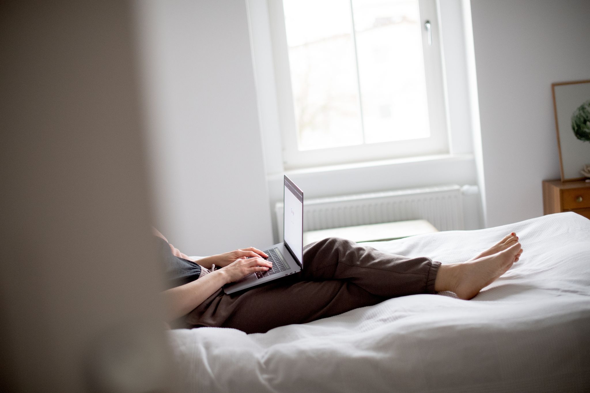 Frau in Jogginghose sitzt auf dem Bett