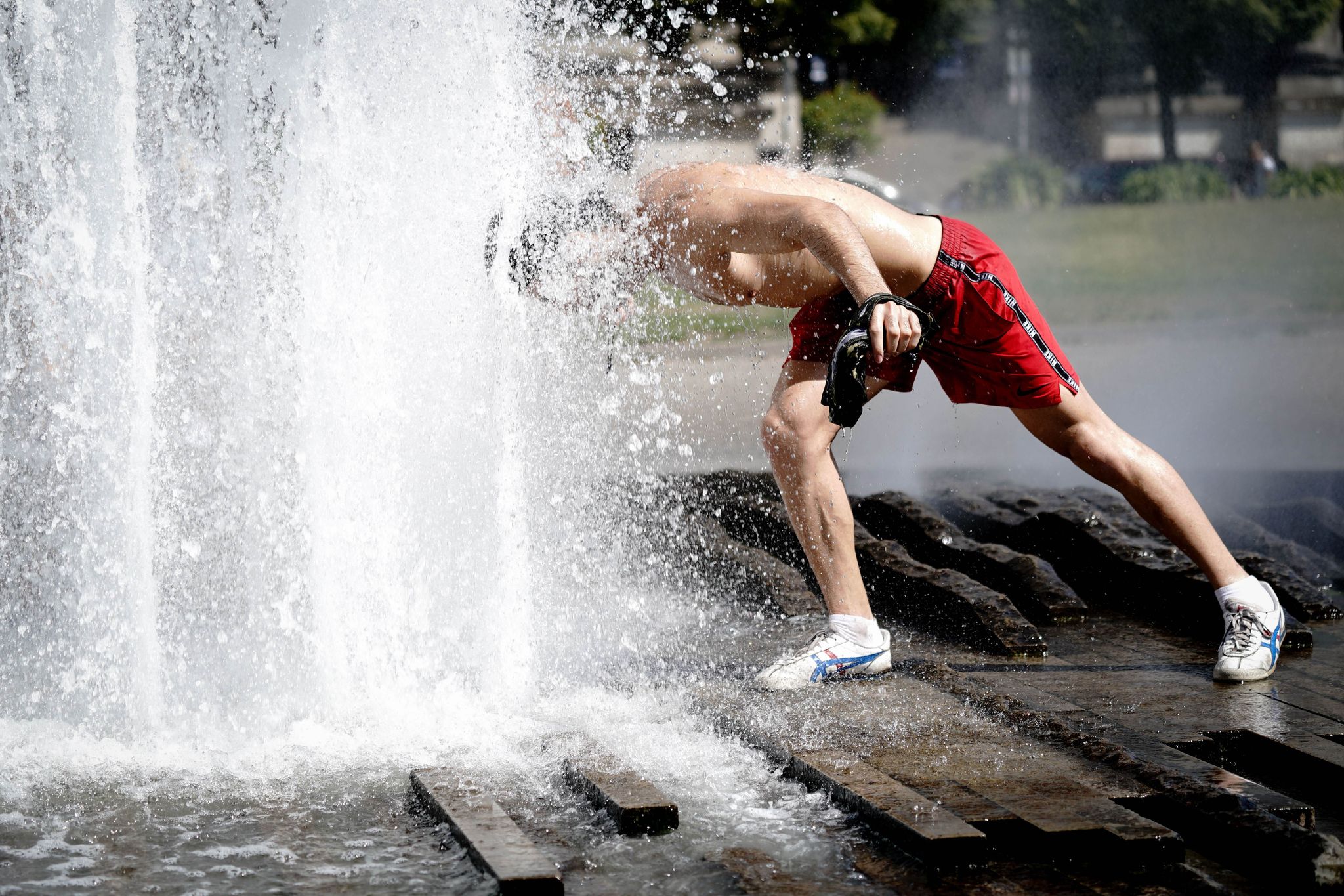 Ein Passant erfrischt sich bei großer Hitze am Brunnen